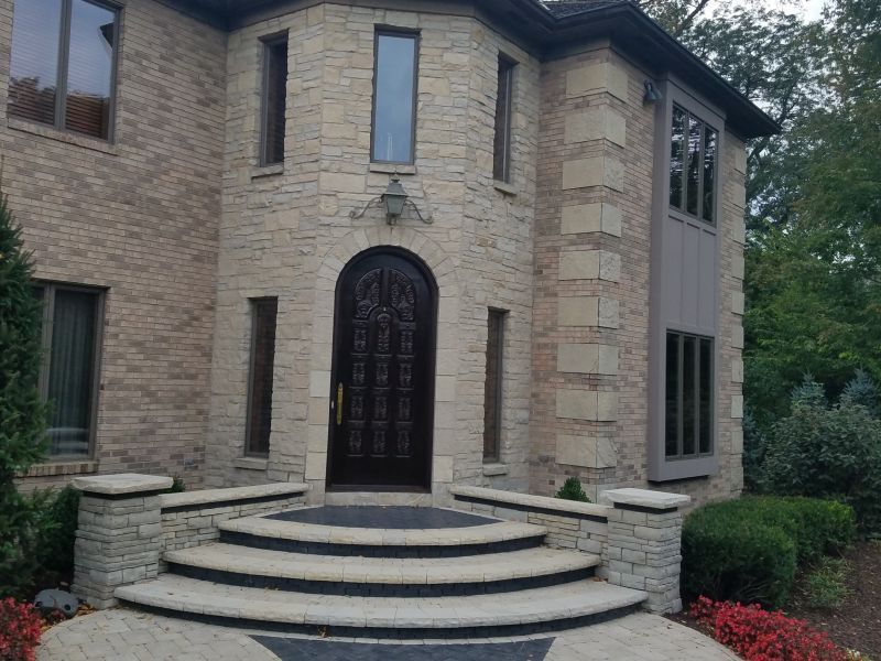 A large, beige stone-clad house with an arched dark wood door, a curved staircase, and several windows.