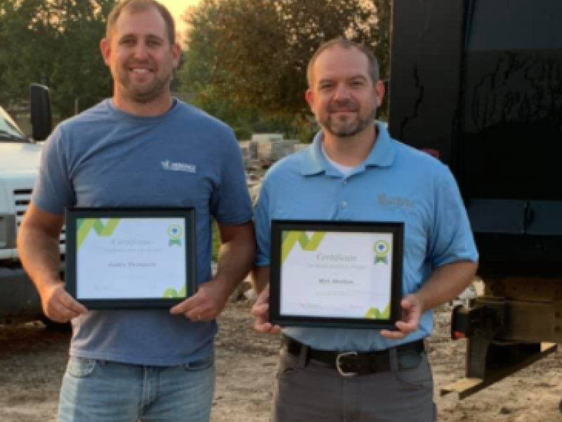Two men holding framed certificates in front of a truck
