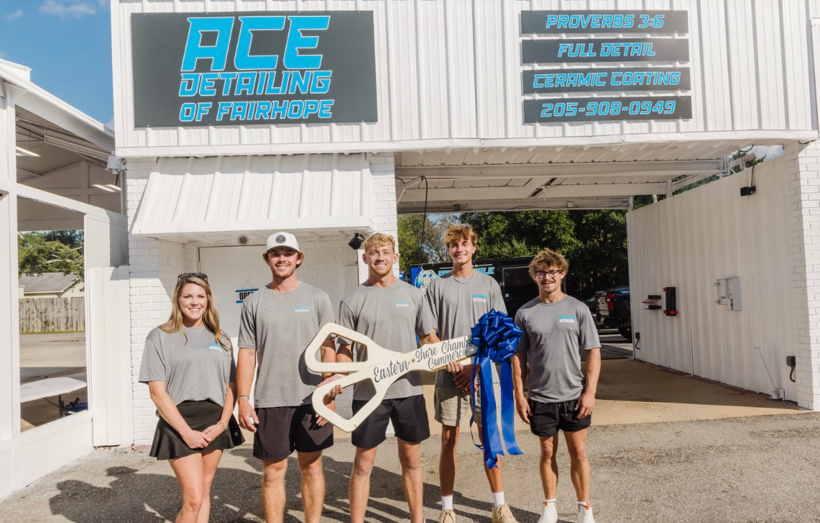 Group of people holding giant scissors in front of a car detailing business.