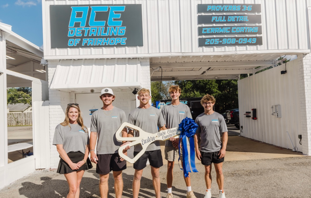 Group of people holding giant scissors in front of a car detailing business.