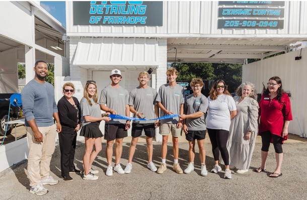 People cutting a blue ribbon in front of a building with the words 