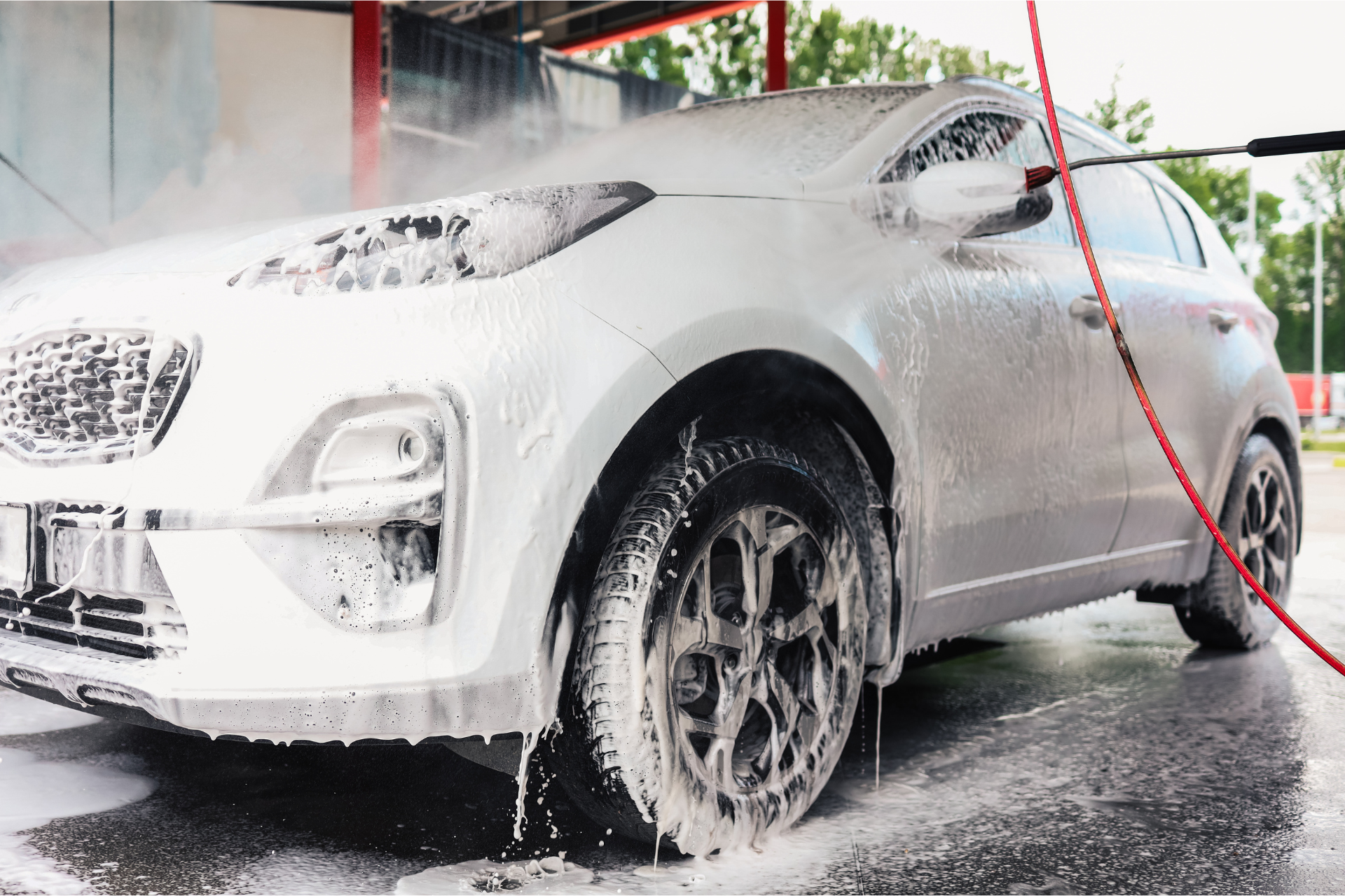 White car being washed at a car wash, covered in soapy foam.