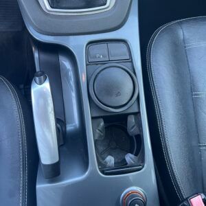 Consolle centrale dell'auto con freno a mano, portabicchieri, pulsante del sensore di parcheggio e manopola girevole.