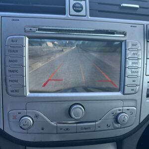 Cruscotto dell'auto con vista della telecamera di retromarcia, che mostra una strada con linee guida rosse.