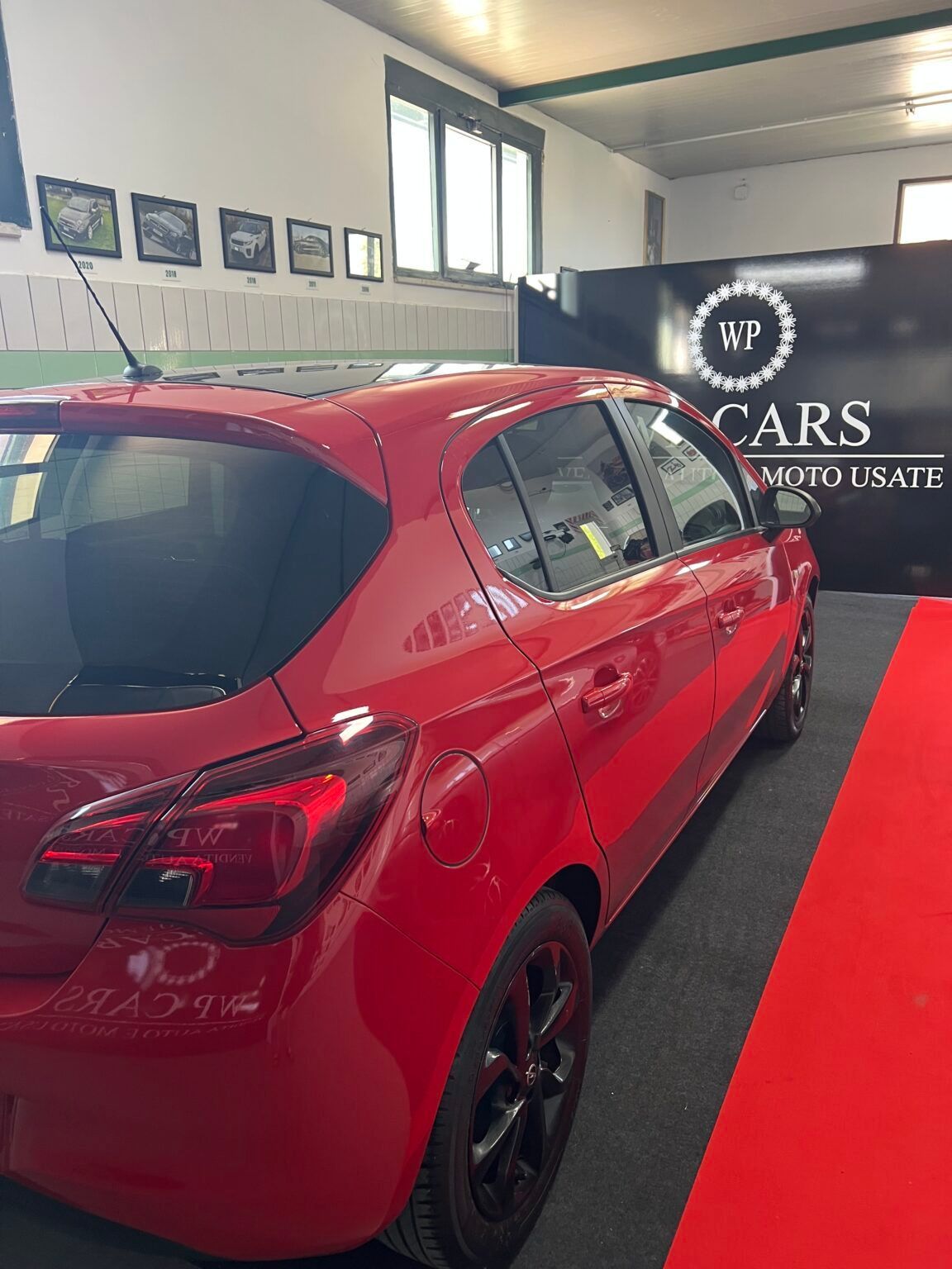 Un'auto rossa parcheggiata su un tappeto rosso all'interno, con il logo della concessionaria sullo sfondo.