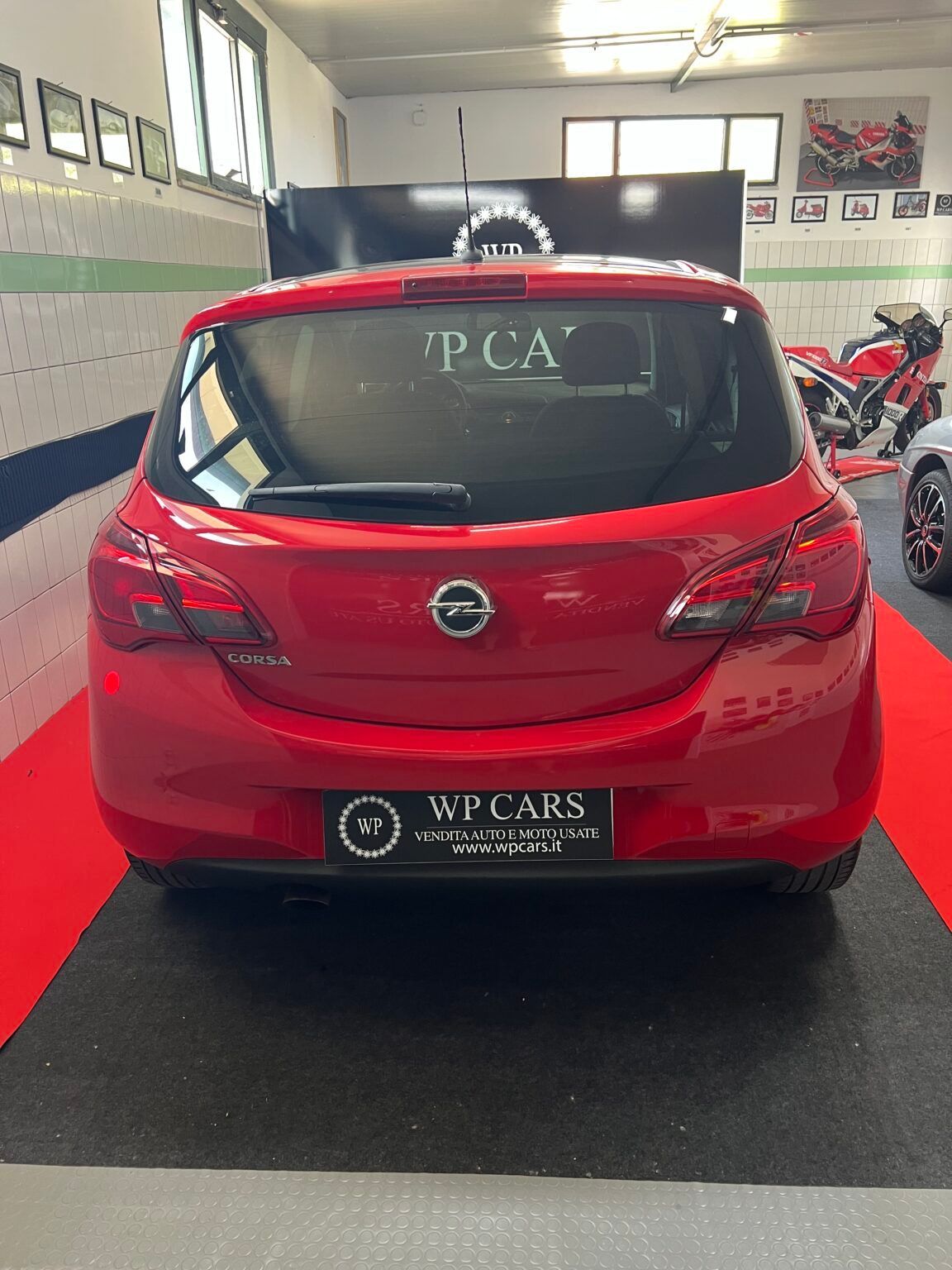 Opel Corsa hatchback rossa in uno showroom automobilistico, vista posteriore.