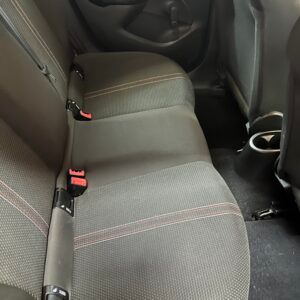 Sedili posteriori dell'auto, tessuto grigio con cuciture rosse, due cinture di sicurezza visibili.