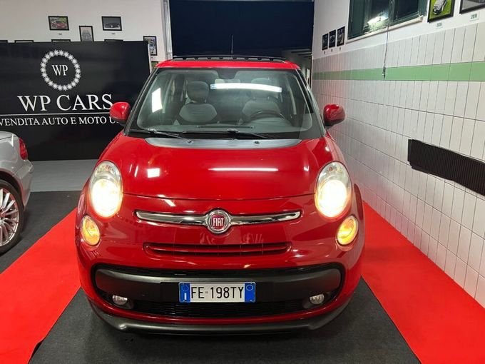 Fiat 500L rossa parcheggiata in uno showroom. Vista frontale con fari accesi. Targa italiana.