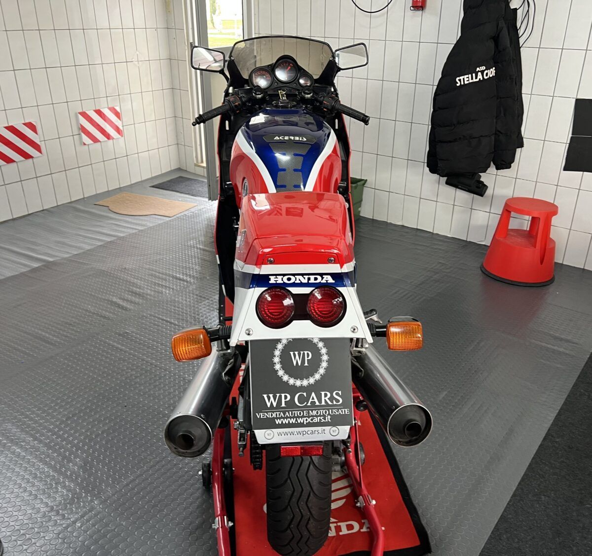 Vista posteriore di una motocicletta Honda rossa, bianca e blu, su un supporto in un garage.