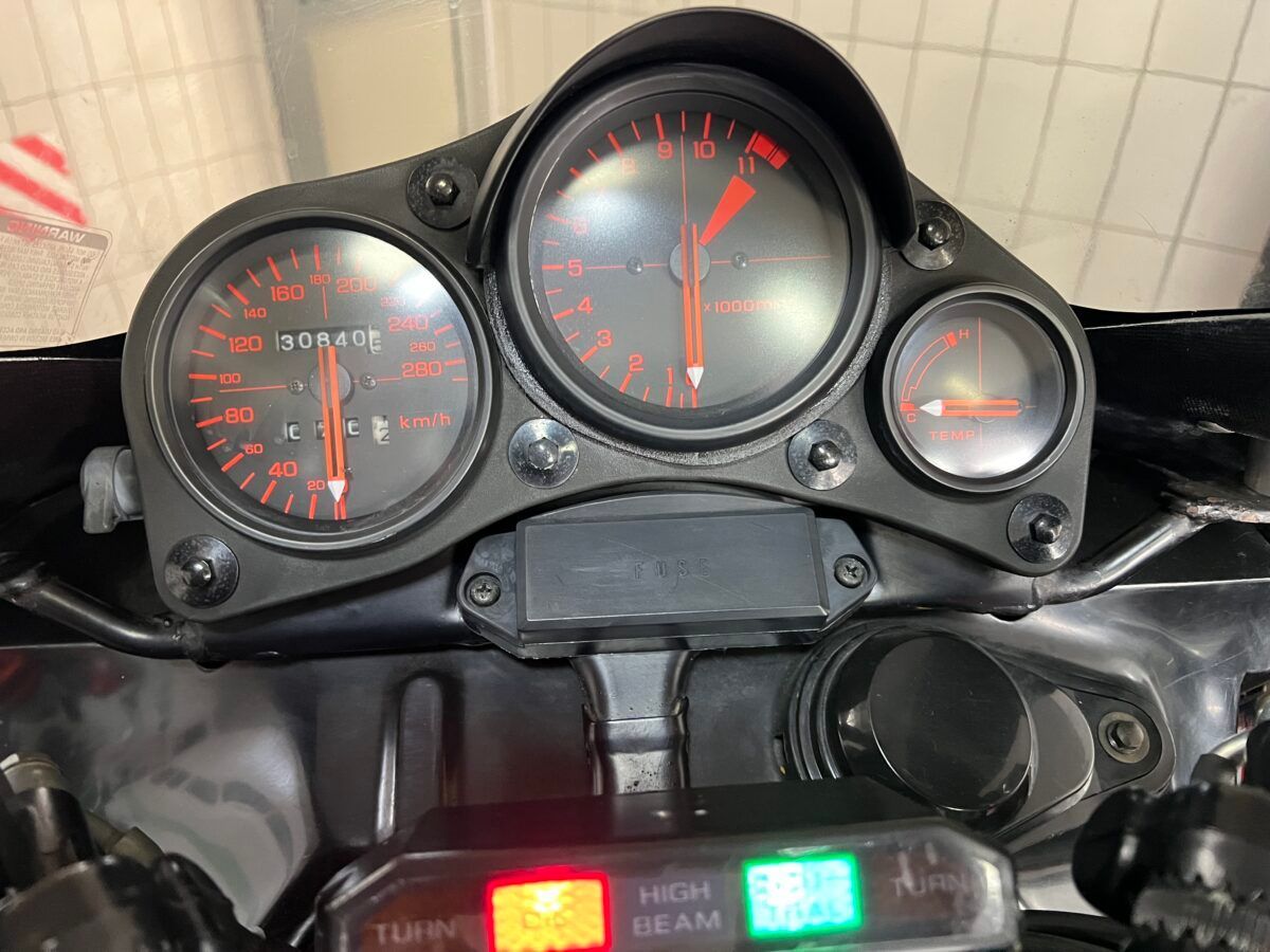 Cruscotto della motocicletta: tachimetro, contagiri, indicatore del livello del carburante con lancette rosse su sfondo nero.