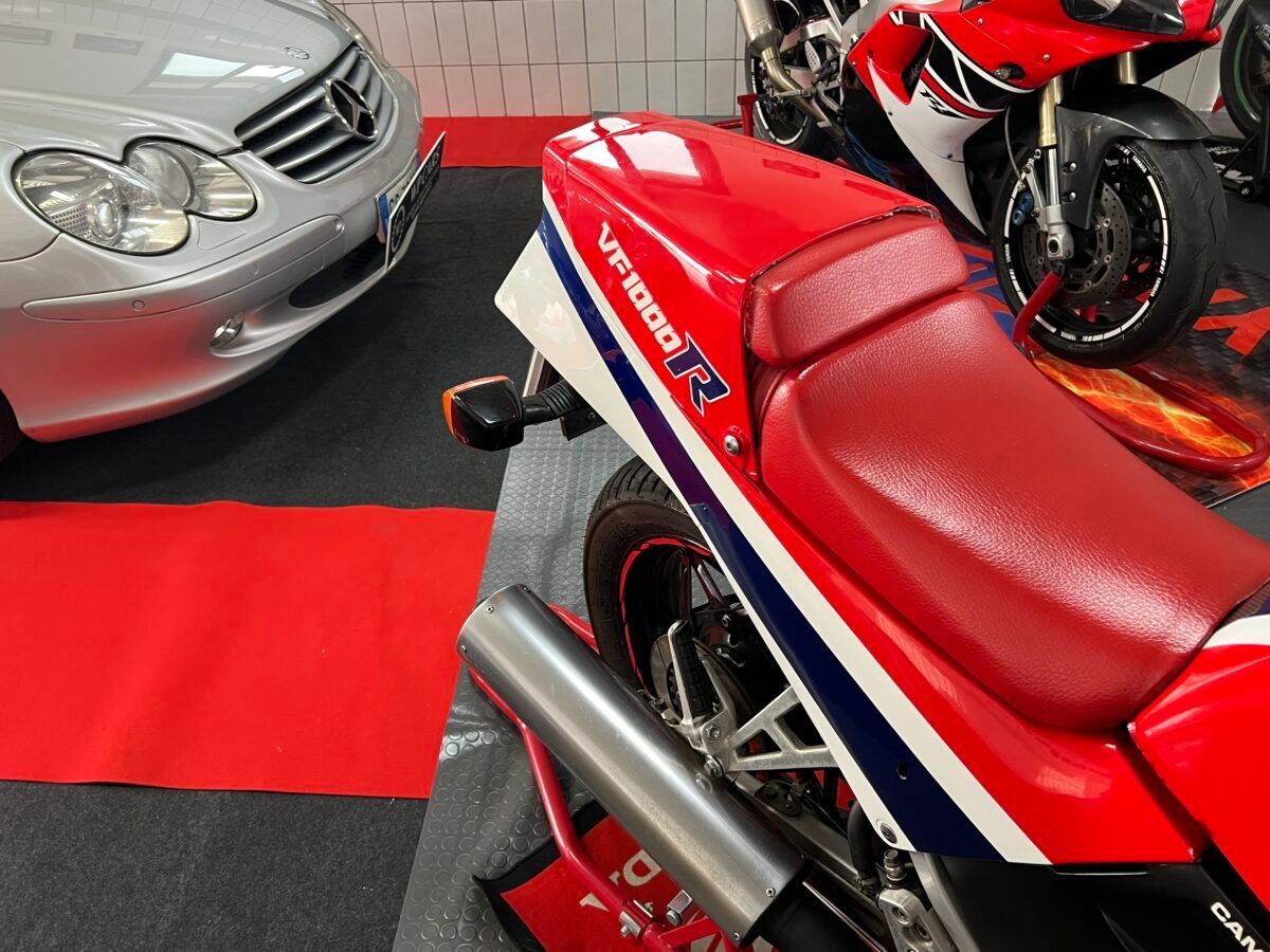 Una motocicletta Honda rossa e bianca, parcheggiata accanto a un'auto argentata in un garage.