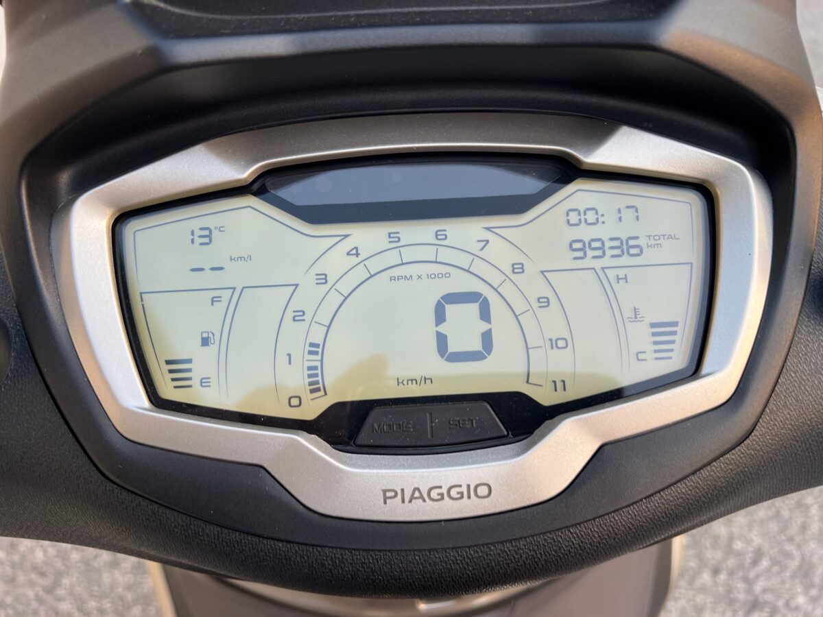 Primo piano del cruscotto digitale di uno scooter Piaggio che mostra velocità, chilometraggio, livelli di carburante e ora.