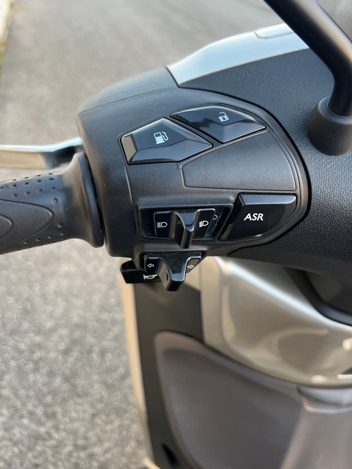 Manubrio dello scooter con pulsanti: carburante, luci, emergenza, ASR (controllo della trazione), indicatori di direzione.