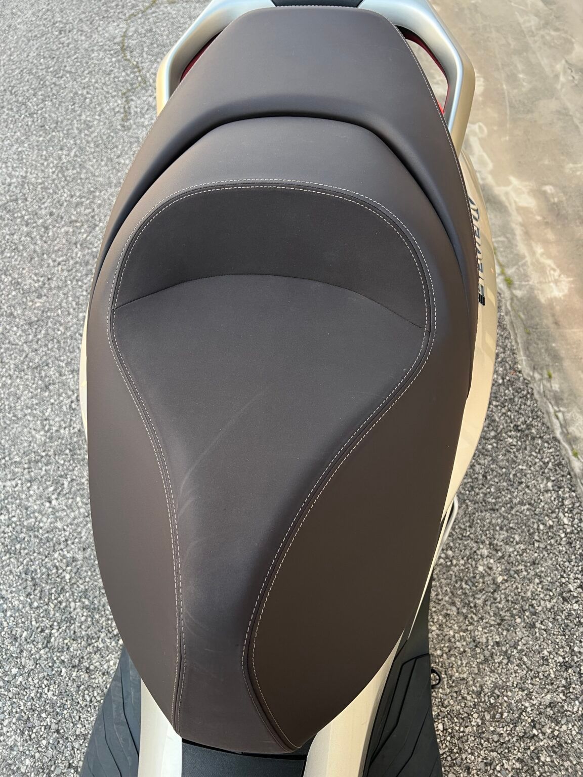 Sedile dello scooter: sedile in pelle marrone con cuciture bianche, vista dall'alto.