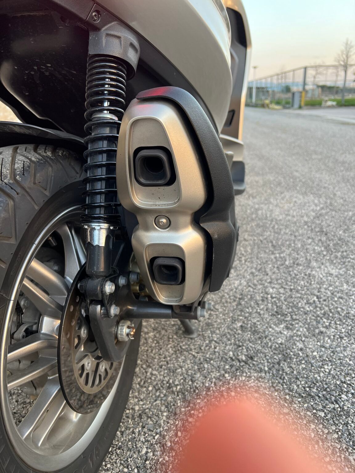 Pneumatico posteriore e sistema di scarico di uno scooter grigio, all'aperto su asfalto.