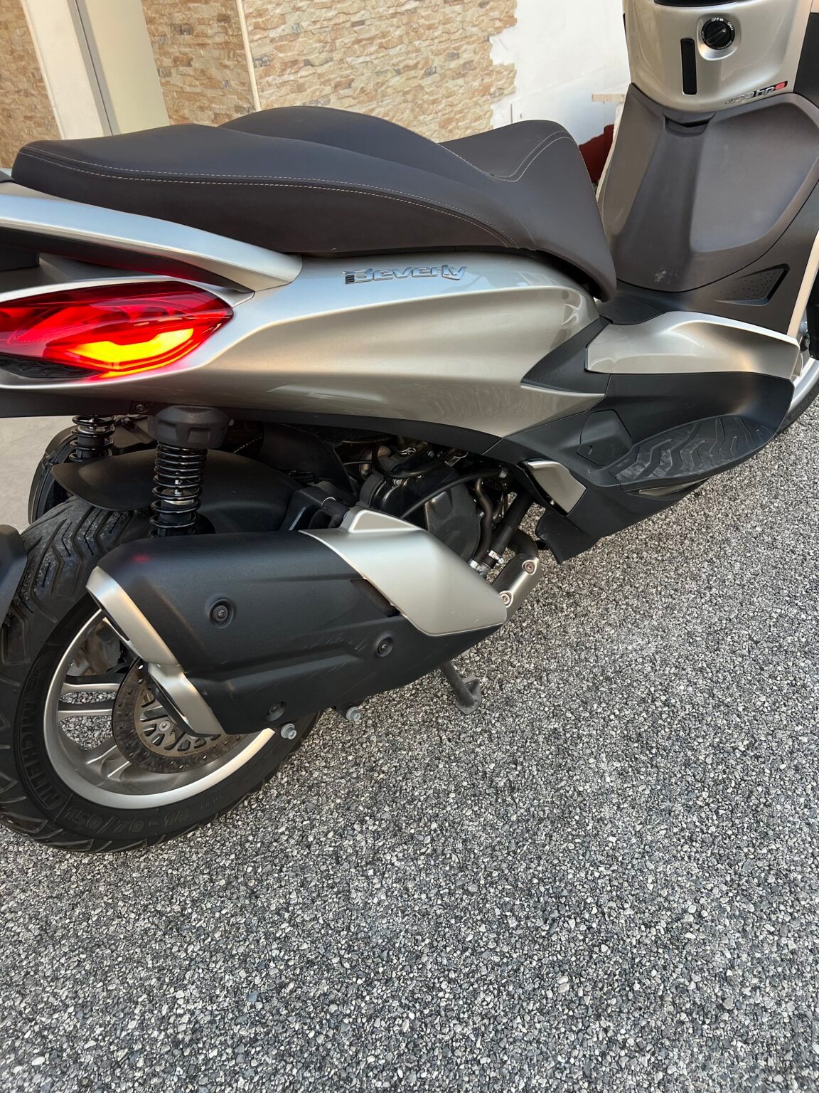 Scooter argentato con sella e scarico neri su superficie ruvida.