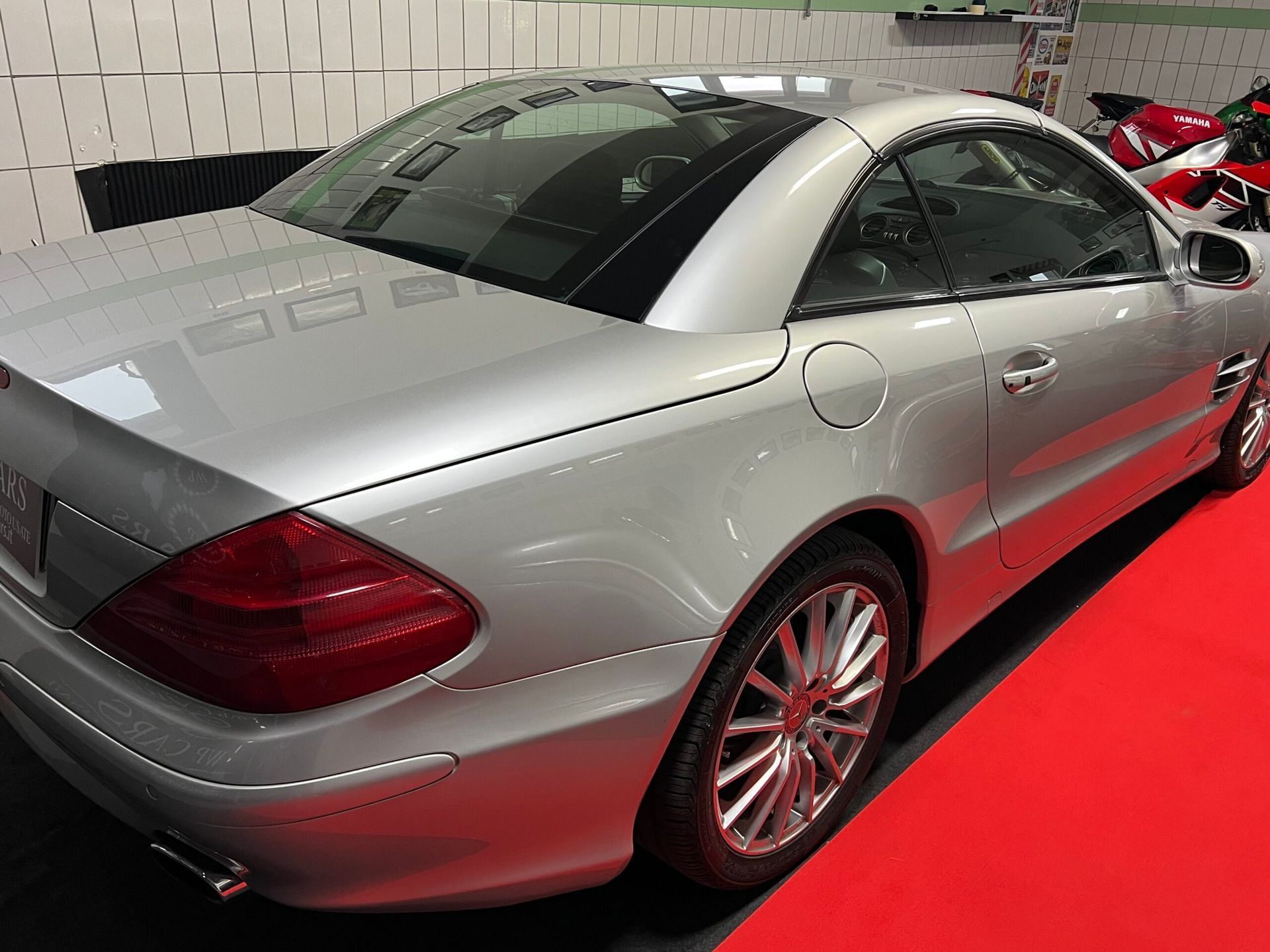 Mercedes-Benz SL decappottabile hardtop color argento parcheggiata su un tappeto rosso in un garage.