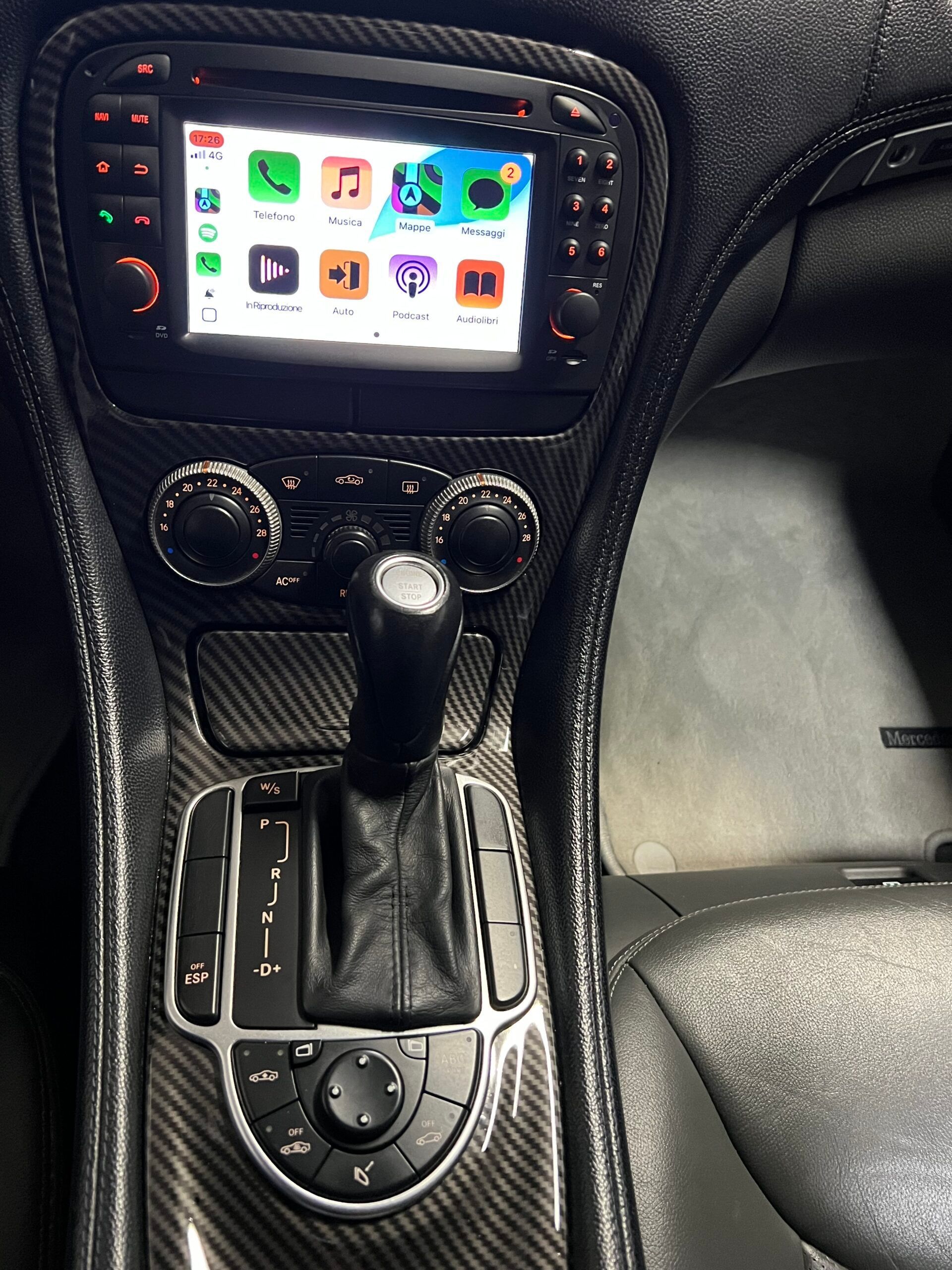 Interno dell'auto con console centrale dotata di cambio, pulsanti e display touchscreen con icone delle app.