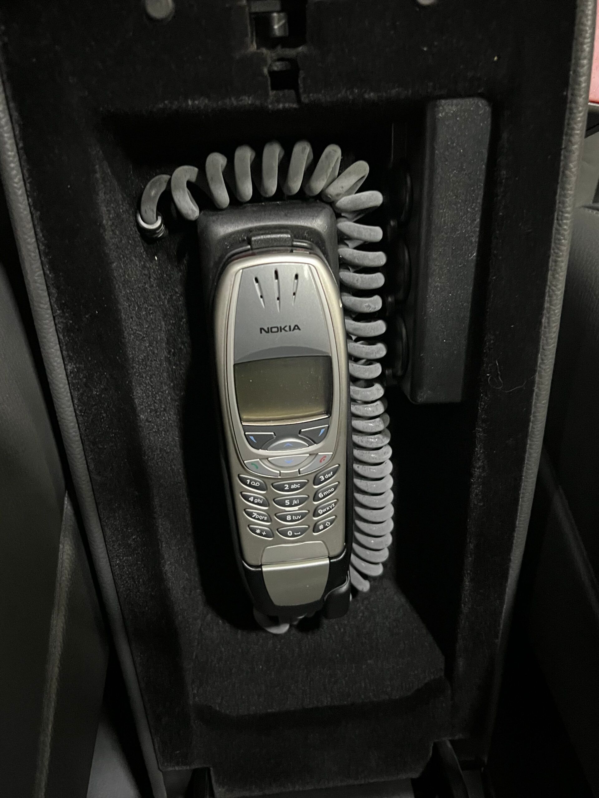 Telefono Nokia nel cruscotto di un'auto, cavo a spirale grigio, interni neri, vintage.