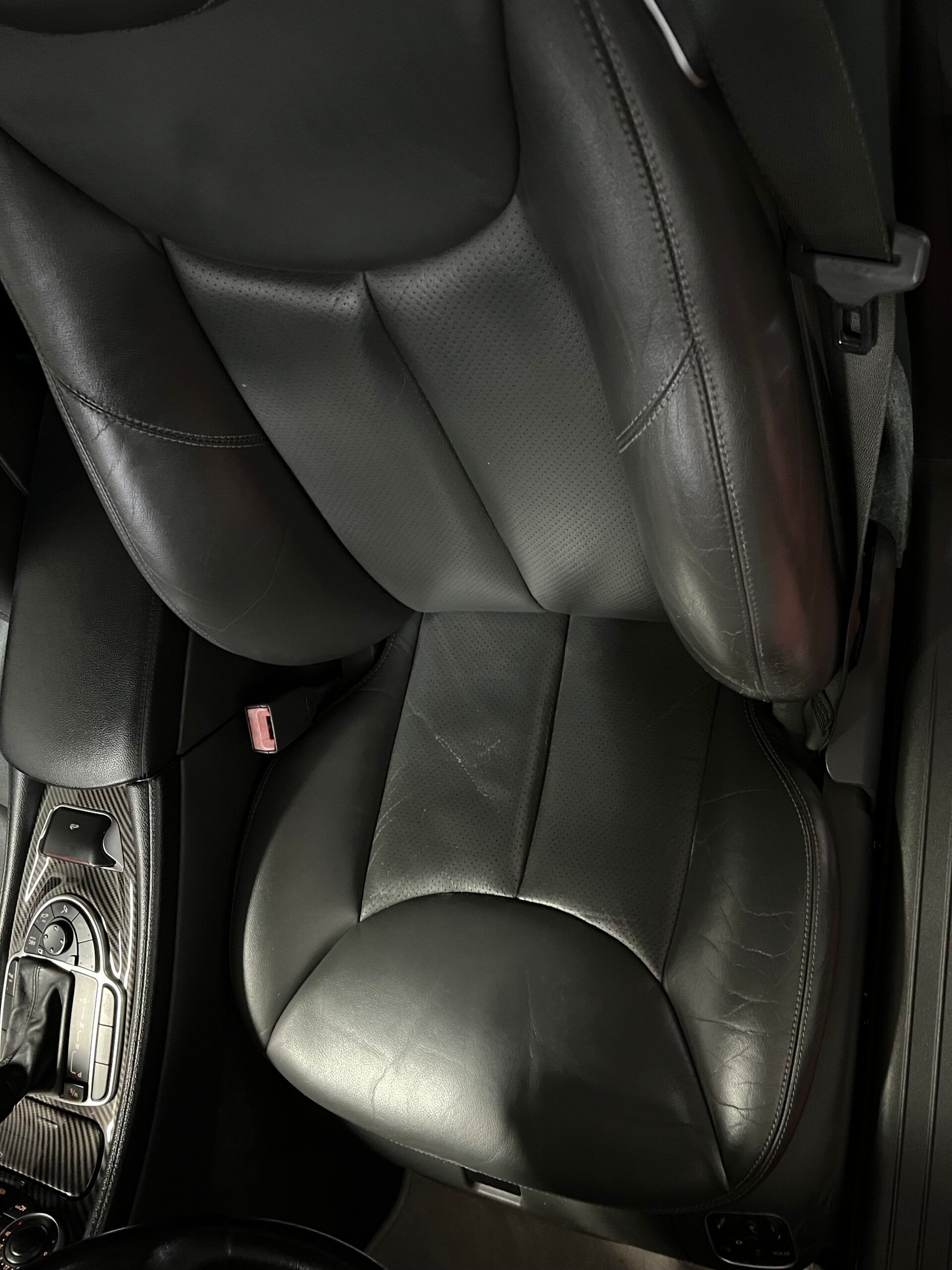 Sedile in pelle nera per auto con segni di usura, probabilmente sedile del conducente.