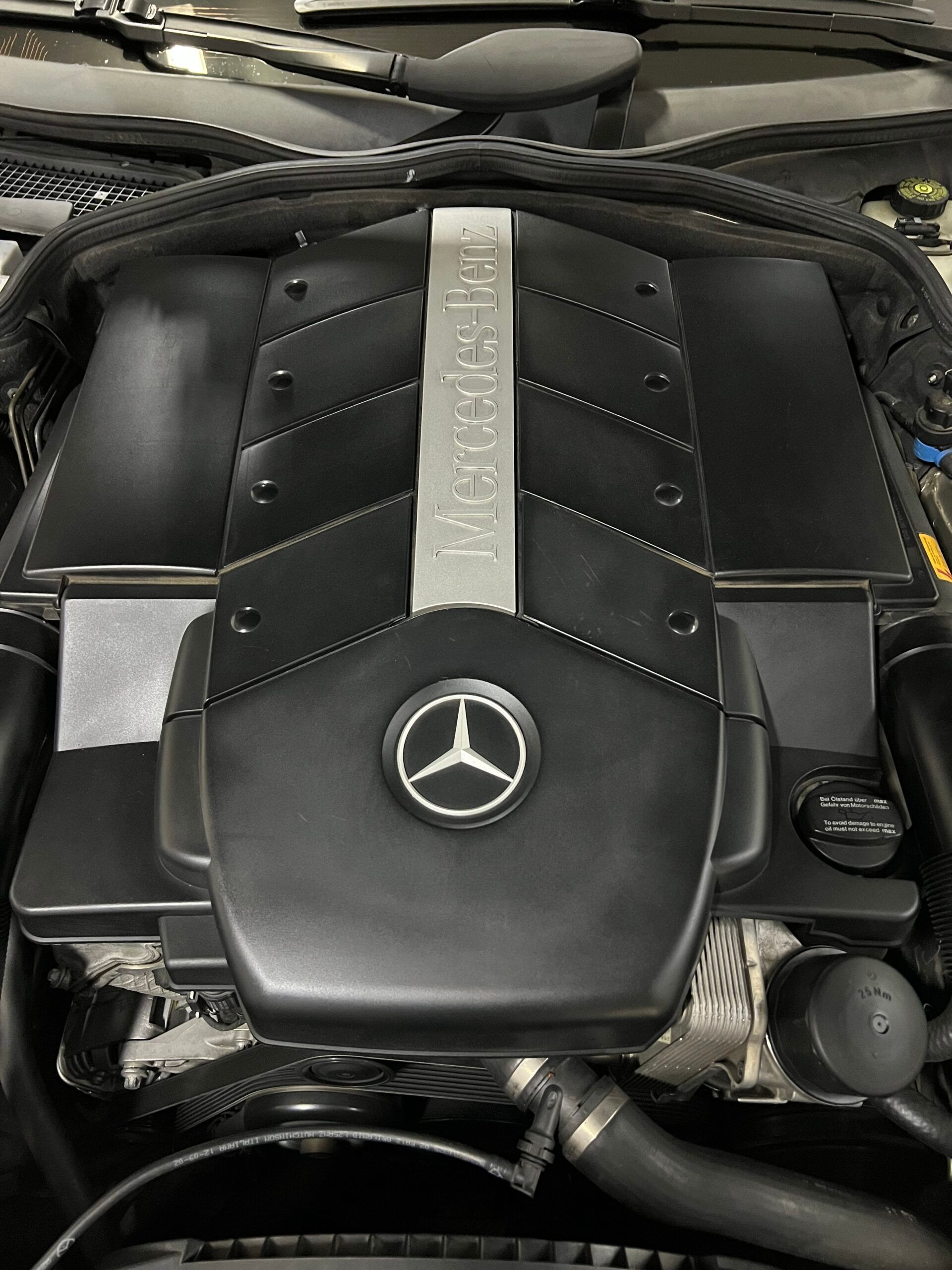 Motore Mercedes-Benz con logo in evidenza e coperchio nero, nel vano motore di un'auto.
