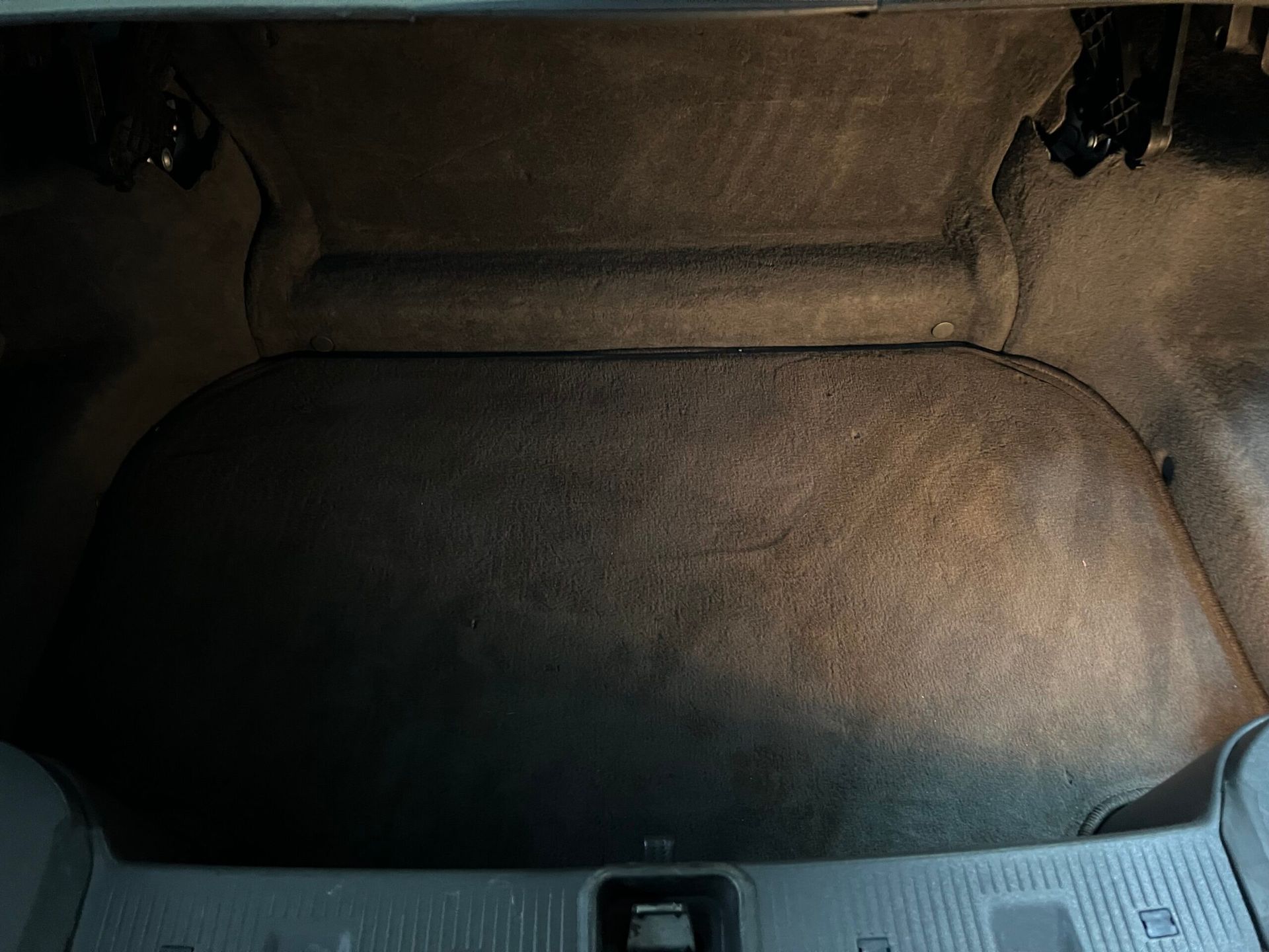 Bagagliaio di un'auto buio e vuoto, con superfici ricoperte di moquette grigia.