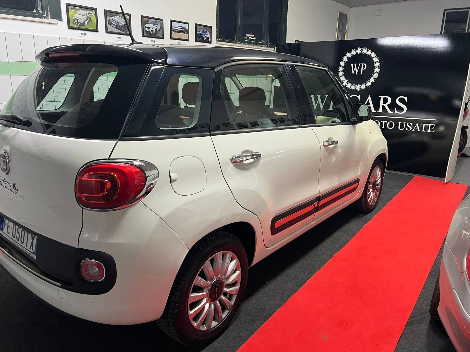 Una Fiat 500L bianca con il tetto nero, parcheggiata su un tappeto rosso in uno showroom.