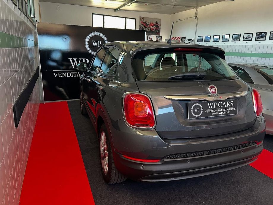 Una Fiat 500X grigia parcheggiata all'interno di uno showroom con moquette rossa.