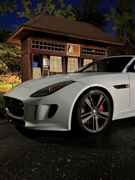 White sports car parked at night beside a wooden building, with a lit cabin in the background