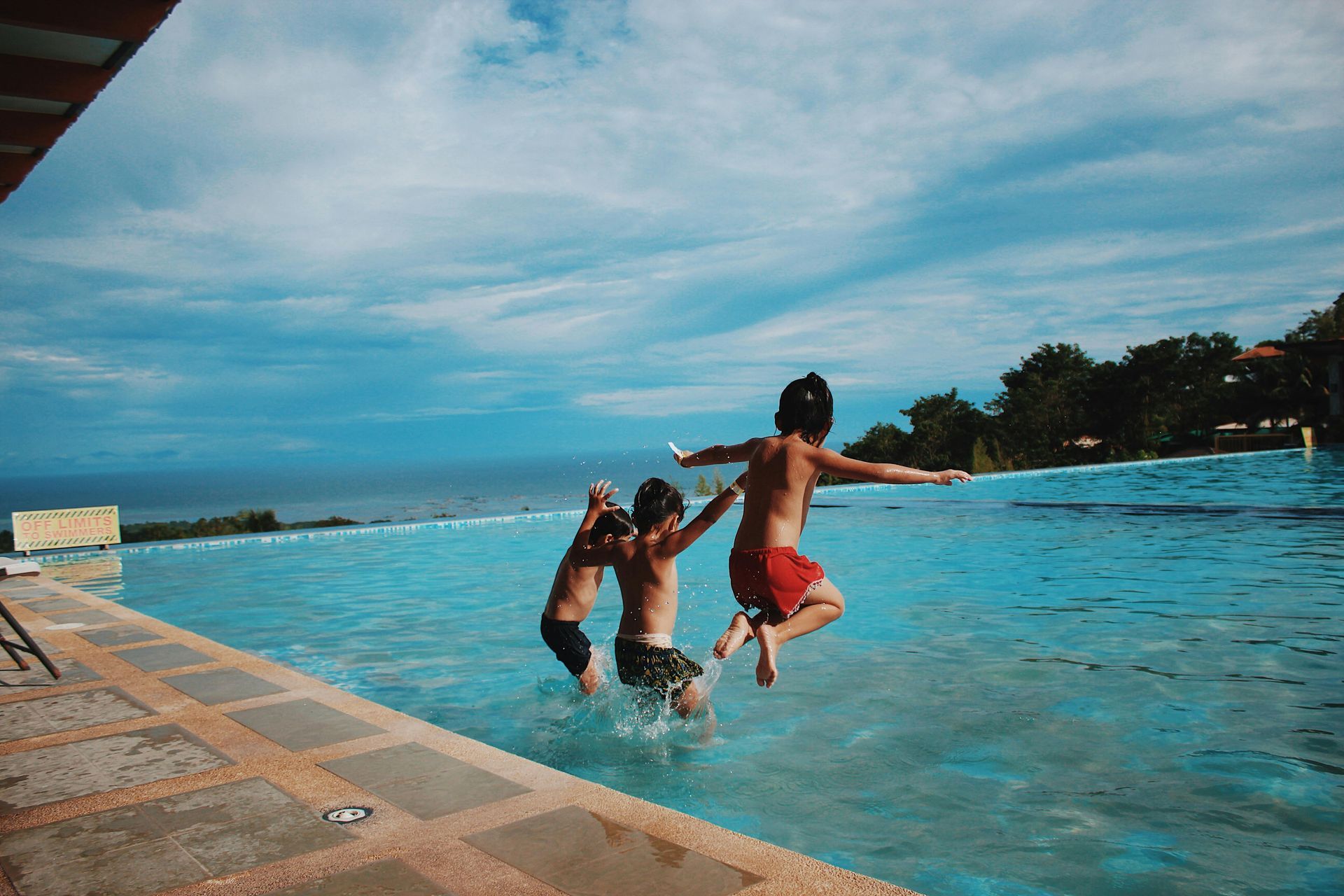 Three children jumping into a sunny infinity pool overlooking the ocean.