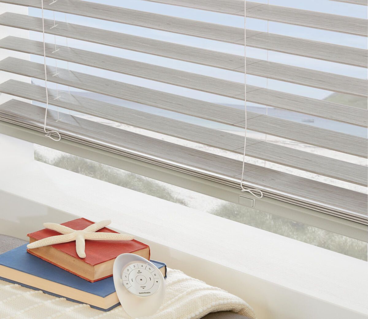 a window with real wood blinds and a starfish on top of a book All Window Decor (817) 448-3393