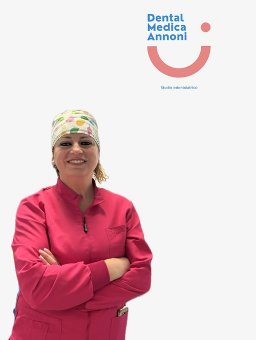 Un professionista del settore dentale, in uniforme rosa e berretto fantasia, sorride con le braccia incrociate, accanto al logo di Dental Medica Annoni.