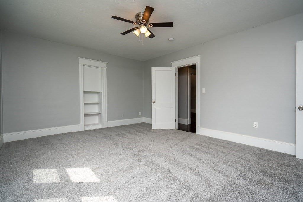an empty room with a ceiling fan and gray carpet
