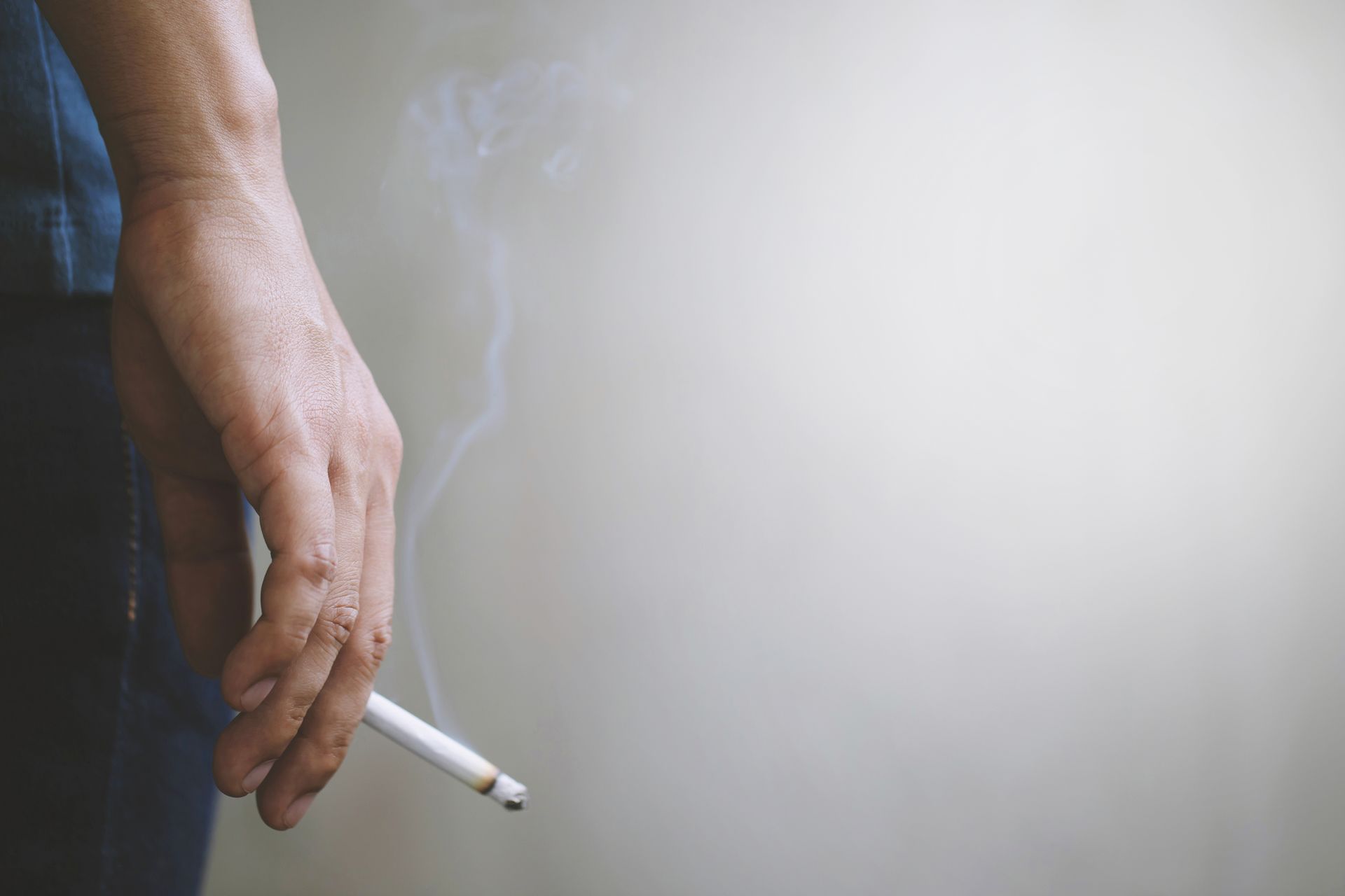 a man's hand holding a burning cigarette between fingers