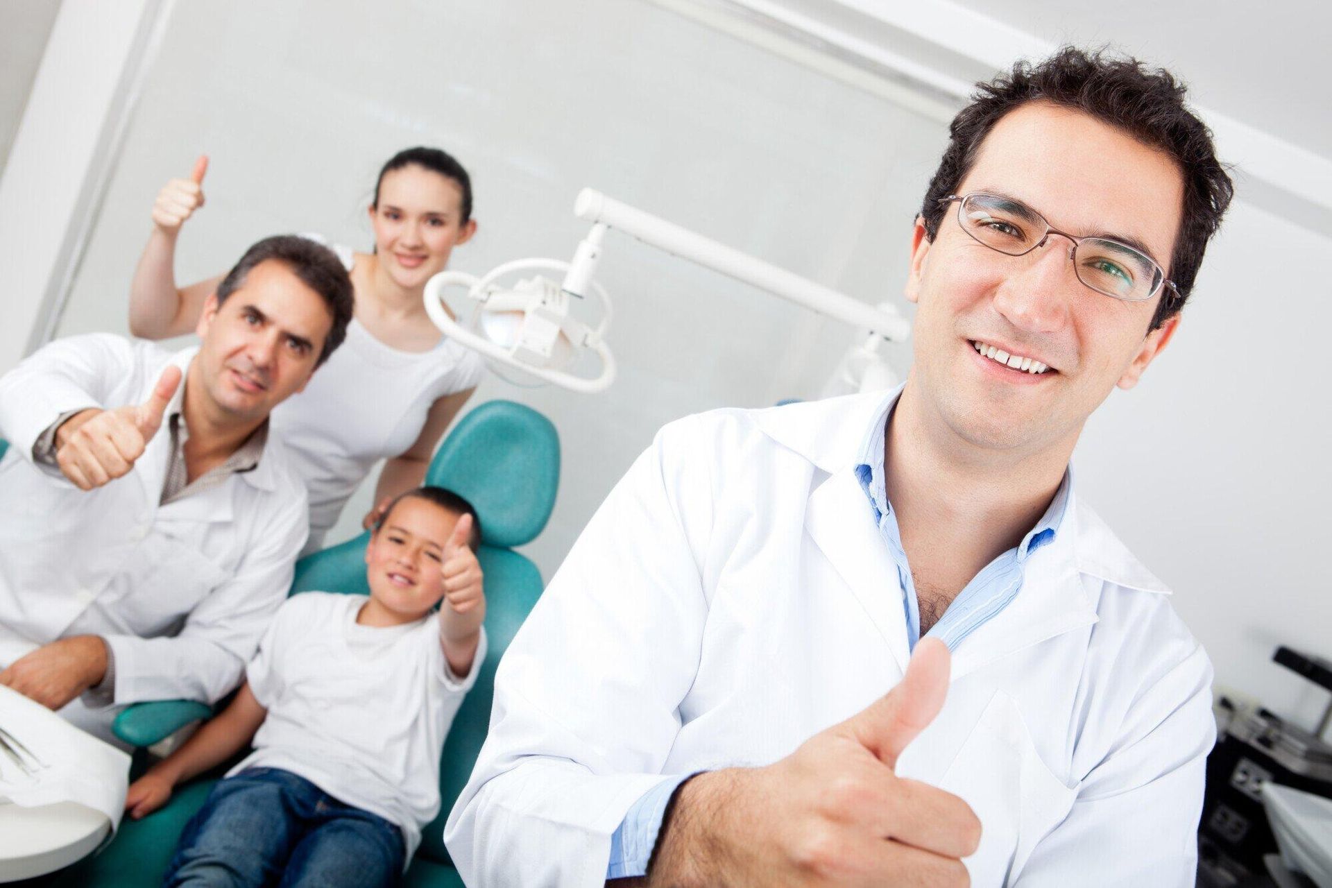 A dentist is giving a thumbs up to a family in a dental chair.