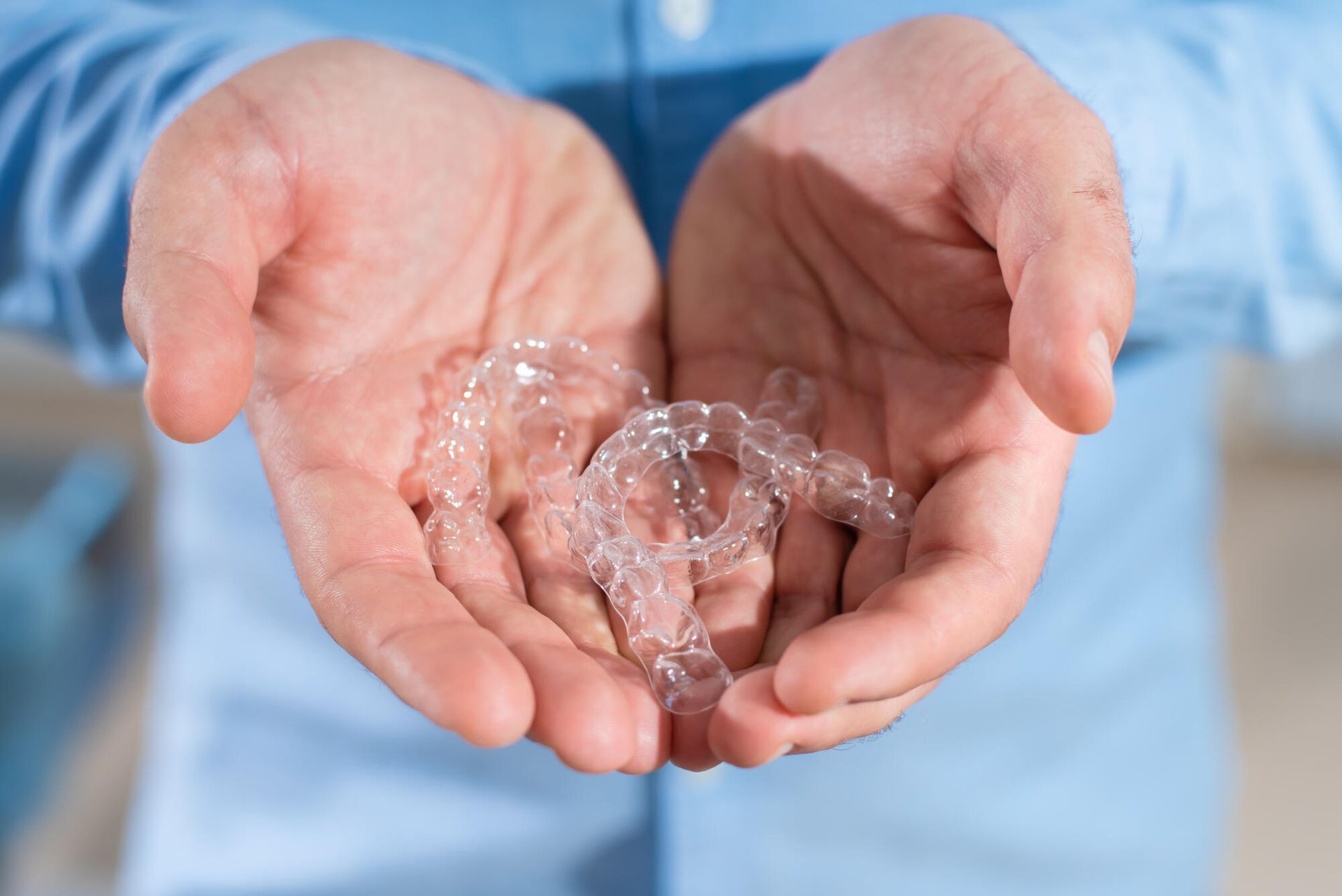 Hands holding clear aligners.