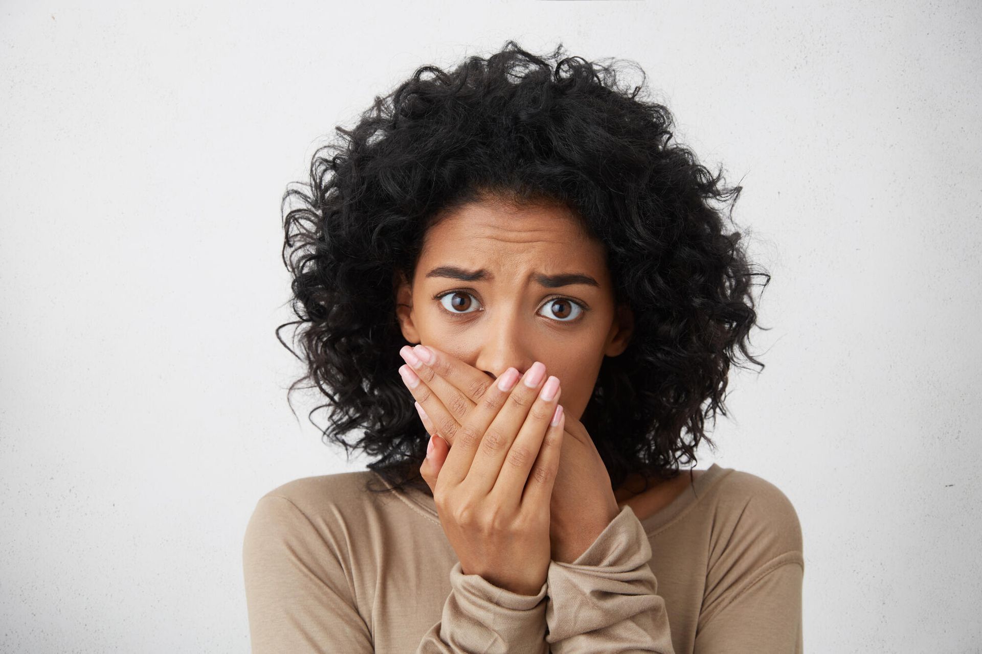 A woman with curly hair is covering her mouth with her hands.