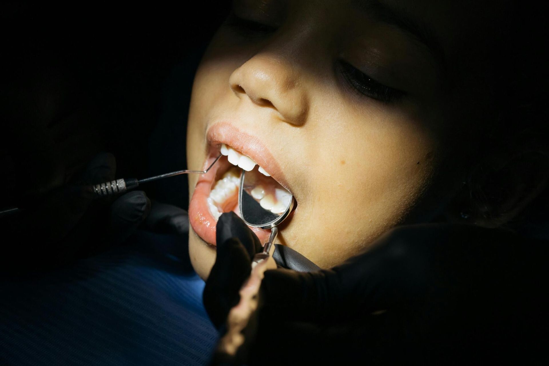 Dentist examining a patient's teeth with a mirror and probe. Mouth open, in a dental office.