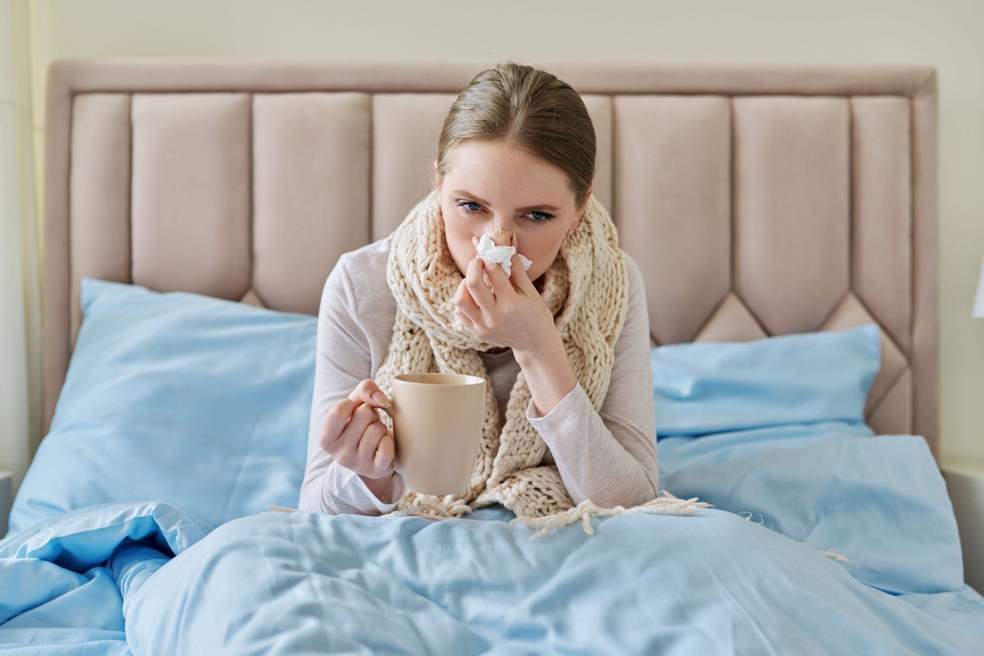 a woman blowing her nose while holding a cup of coffee