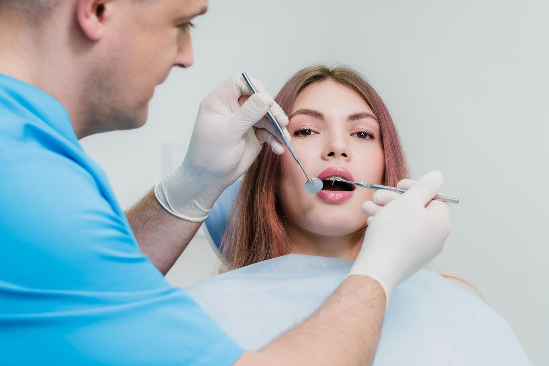 Dentist examining a woman's teeth with tools in a dental office.