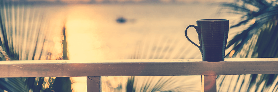 A cup of coffee is sitting on a railing overlooking a body of water.