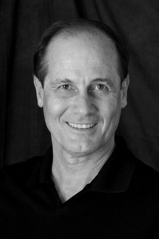 A man in a black shirt is smiling in a black and white photo.