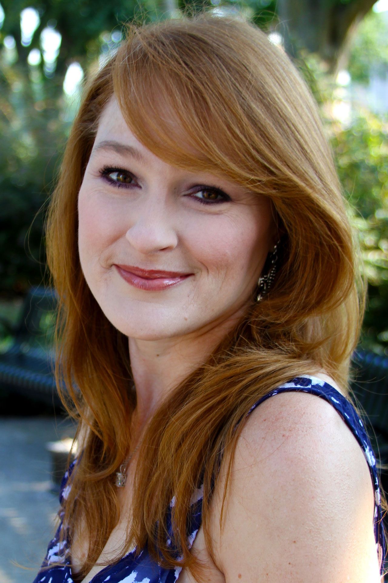 A woman with red hair and a blue dress is smiling for the camera.