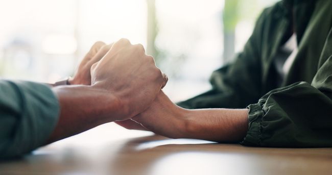 Two people holding hands across a wooden table, offering comfort and support.