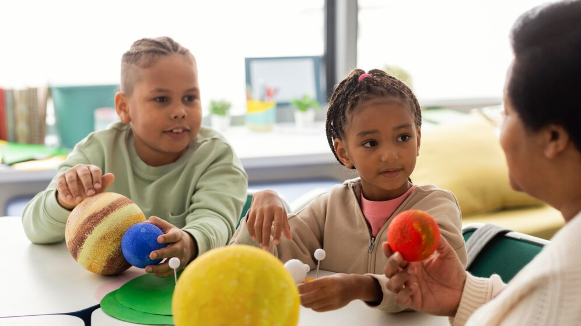A woman is sitting at a table with two children holding balls.