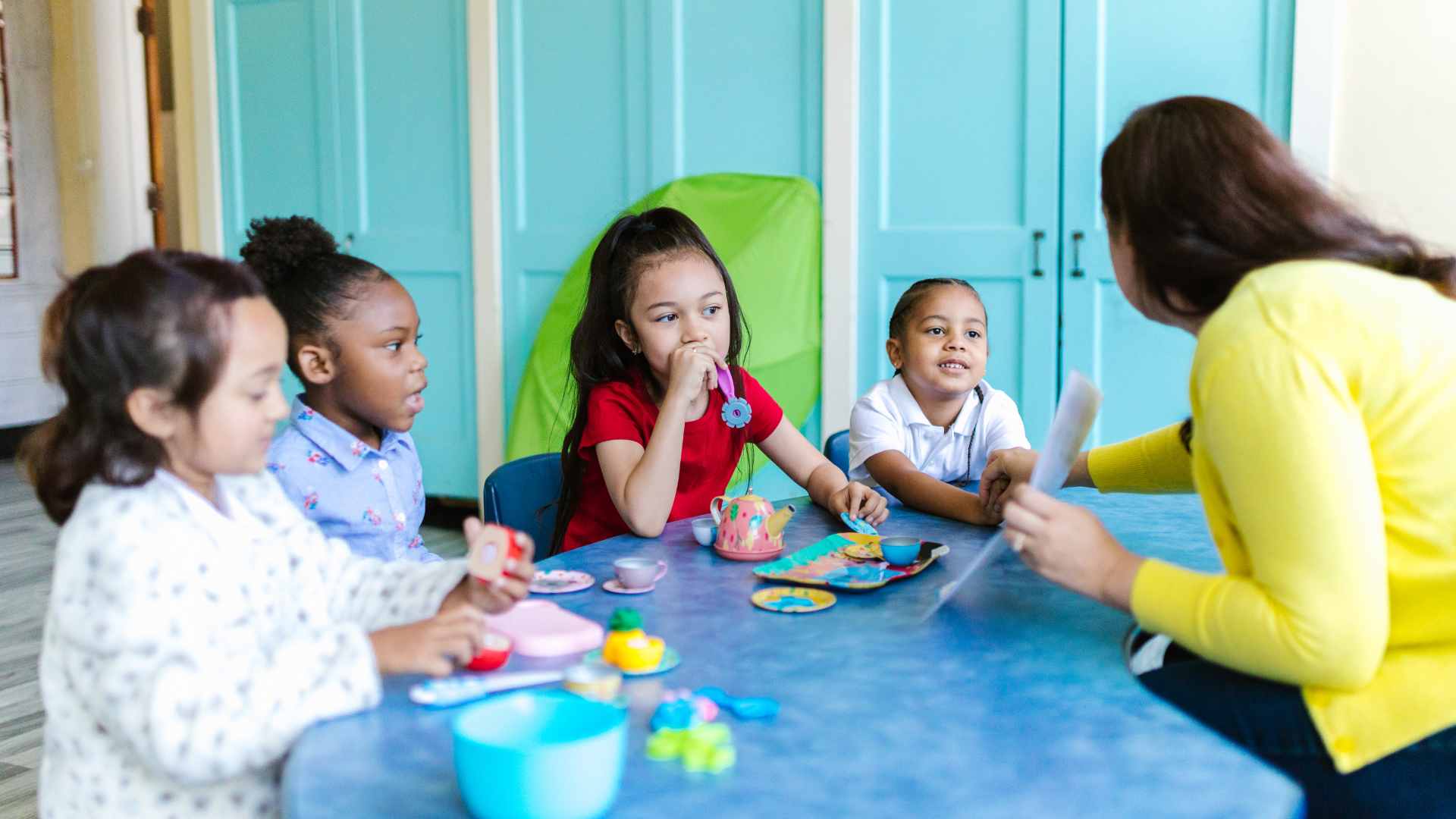 A group of young girls are sitting at a table with a teacher.