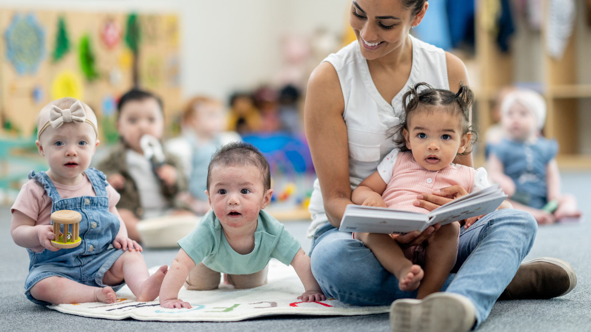 A woman is sitting on the floor reading a book to a group of babies.