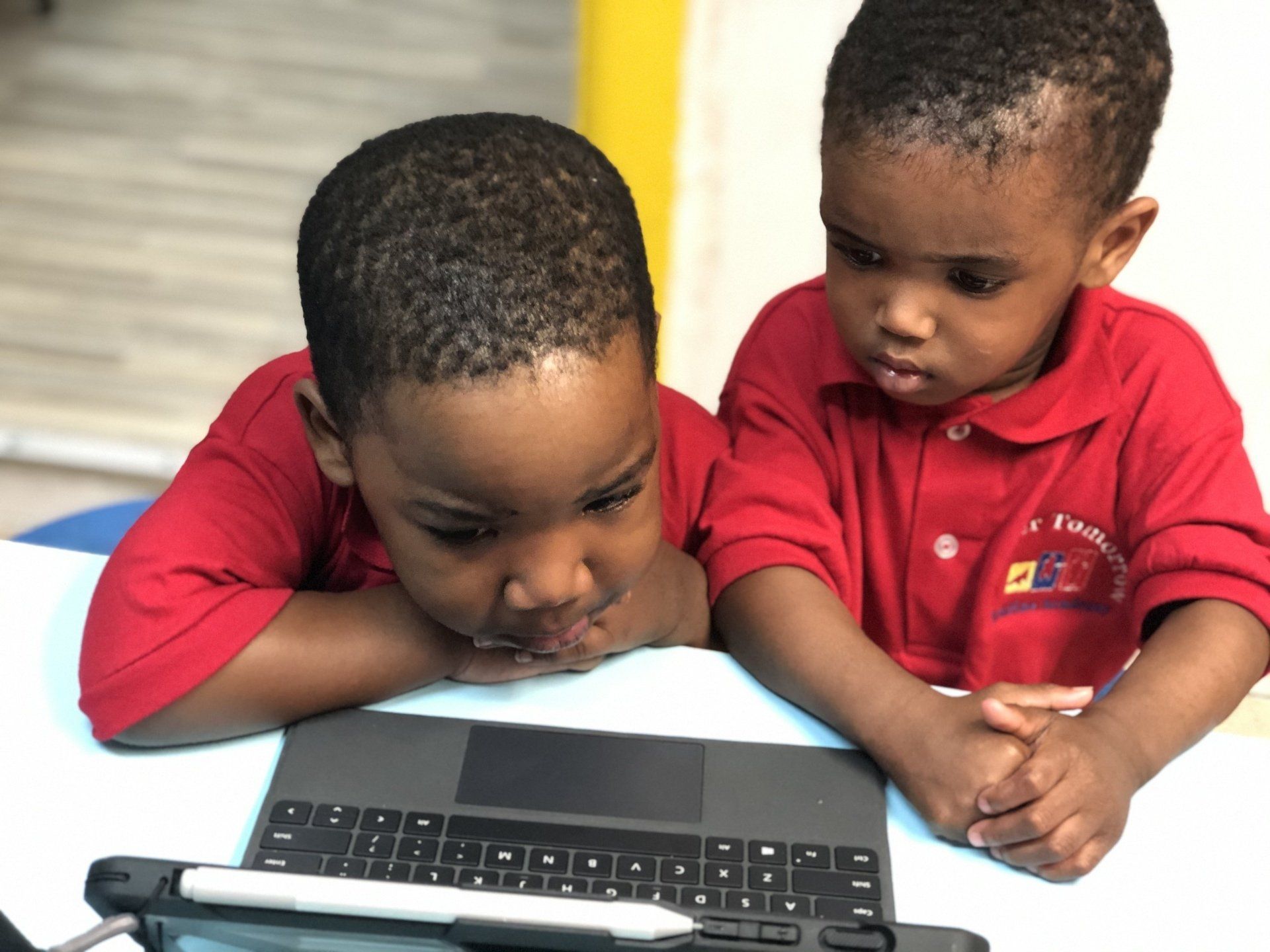 Two young boys in red shirts are looking at a tablet