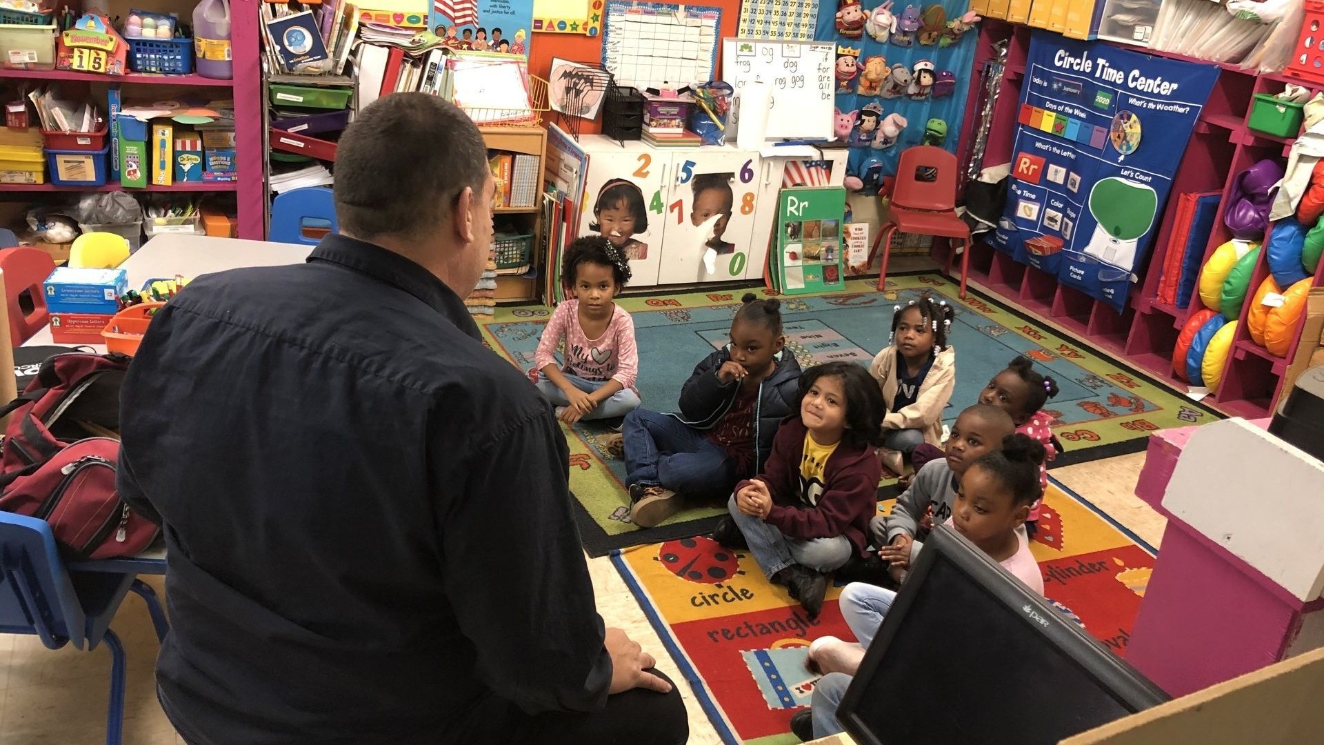 Man reading to a group of children in a classroom.