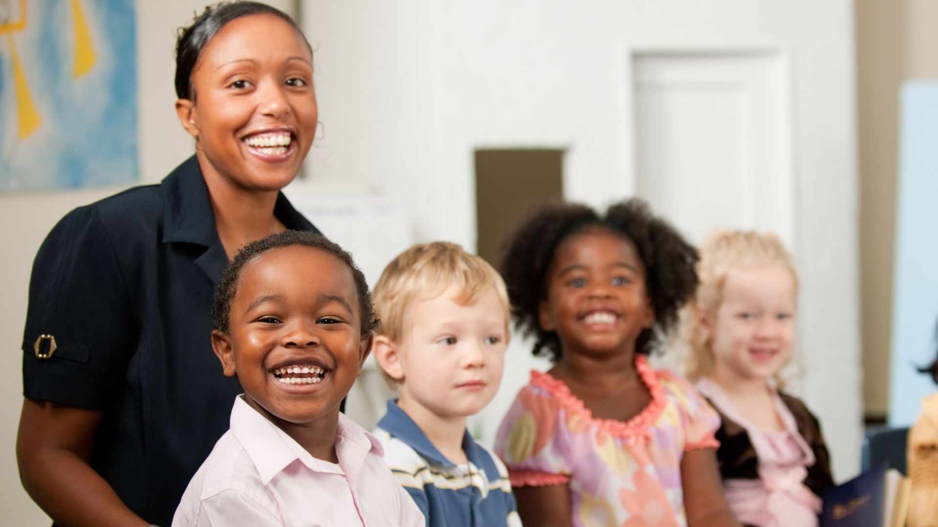 Teacher smiles with a group of children in a classroom.